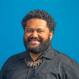 Koroi smiling wearing a dark shirt and necklace.