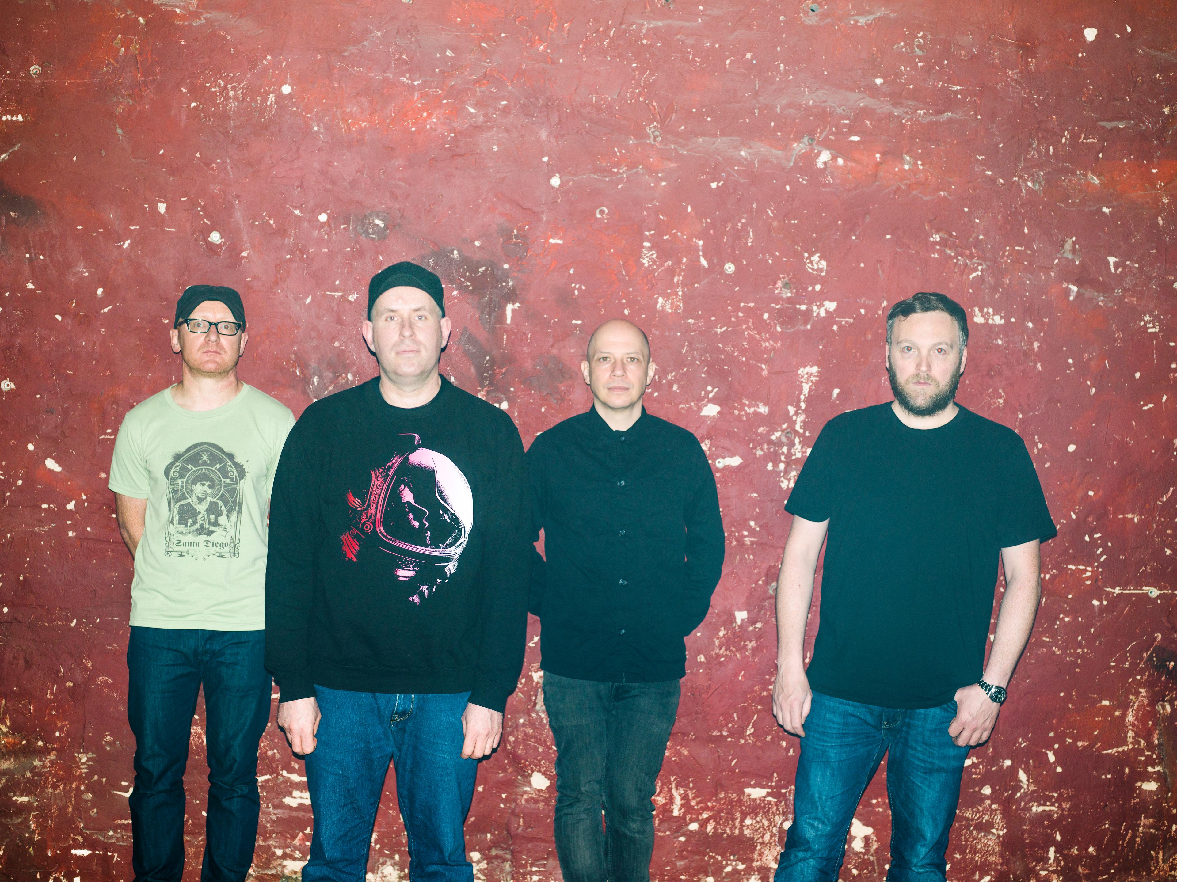 Members of Scottish band Mogwai are standing in a line against a red background.