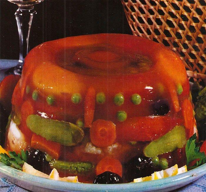 A close up photo of a 70s dish in which carrots, peas and other vegetables are encased in a mound of jelly.