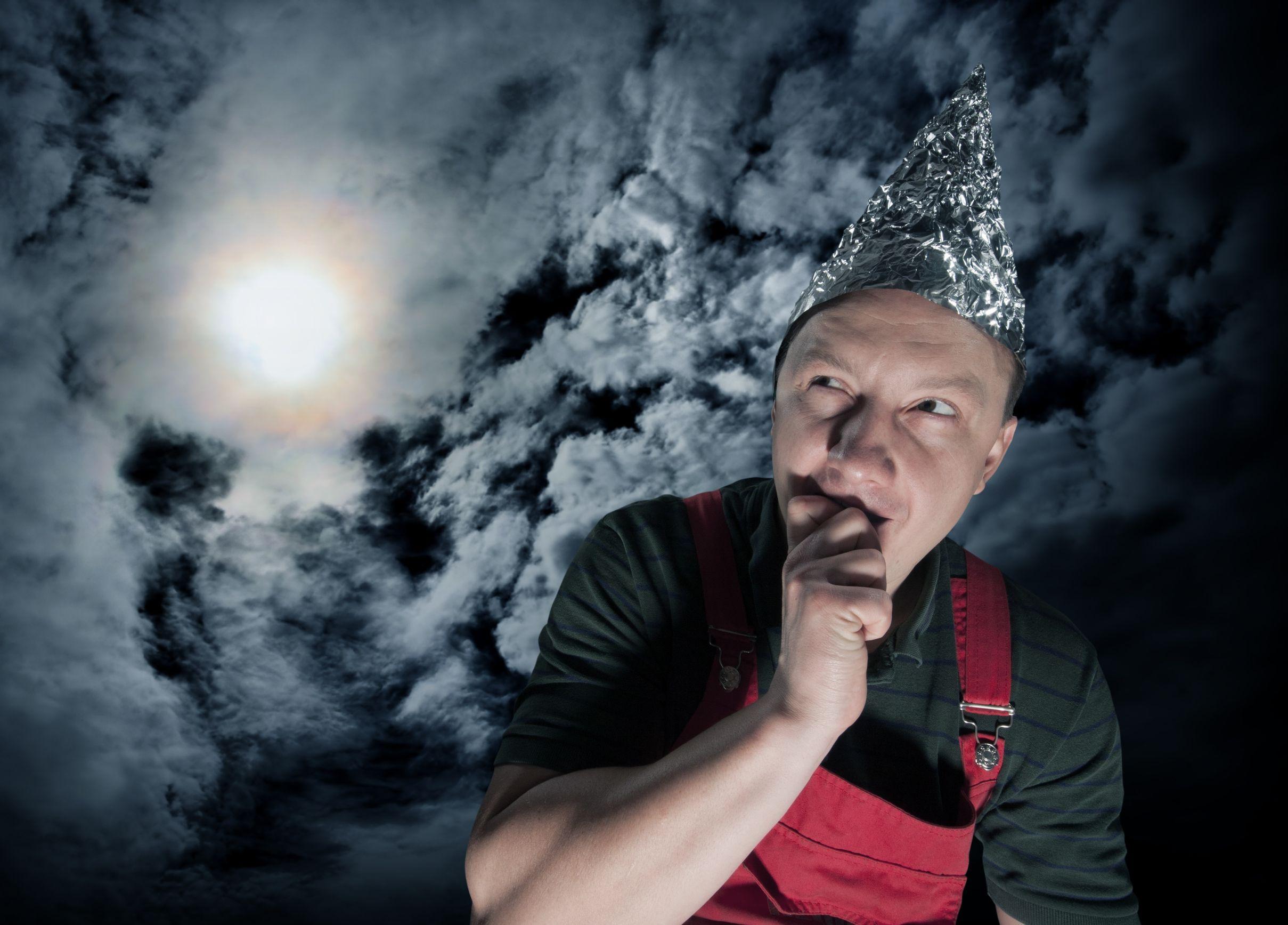 A suspicious man wears a tinfoil hat against a stormy sky.