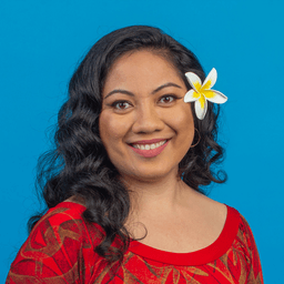 Susana looks directly forward smiling and wearing a flower behind her left ear