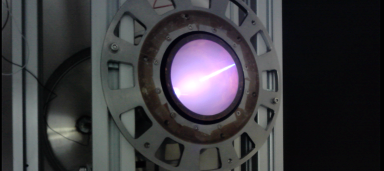 A large metal cylinder embedded in beams with a glowing purple light emanating from its centre.