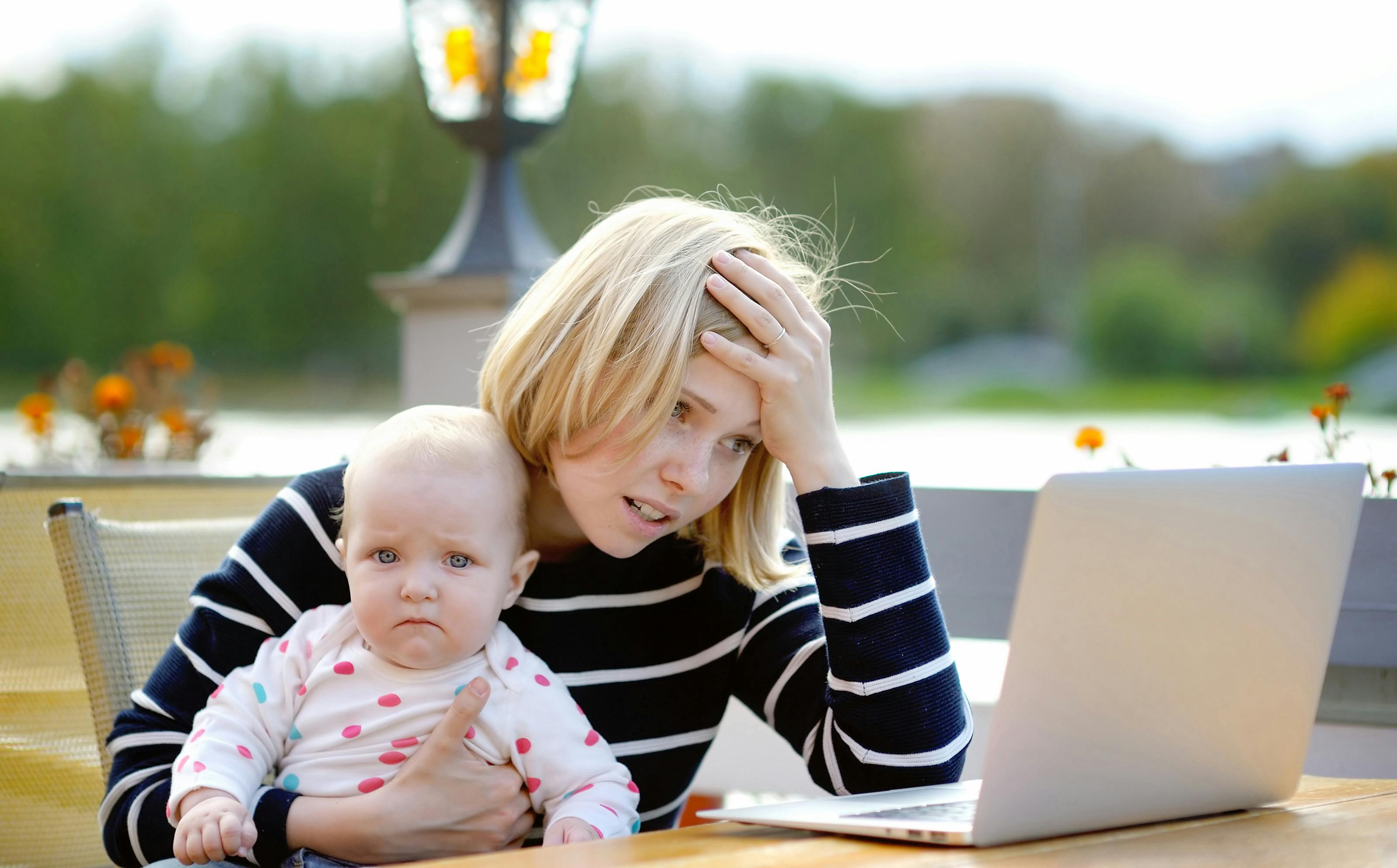 Tired young mother working oh her laptop and holding 6-month daughter