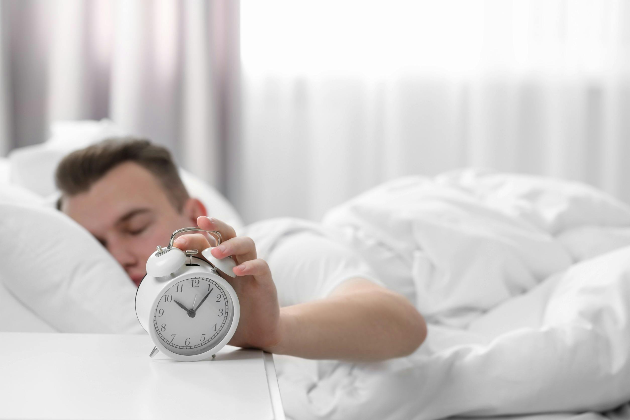 Man sleeping and turning off alarm clock