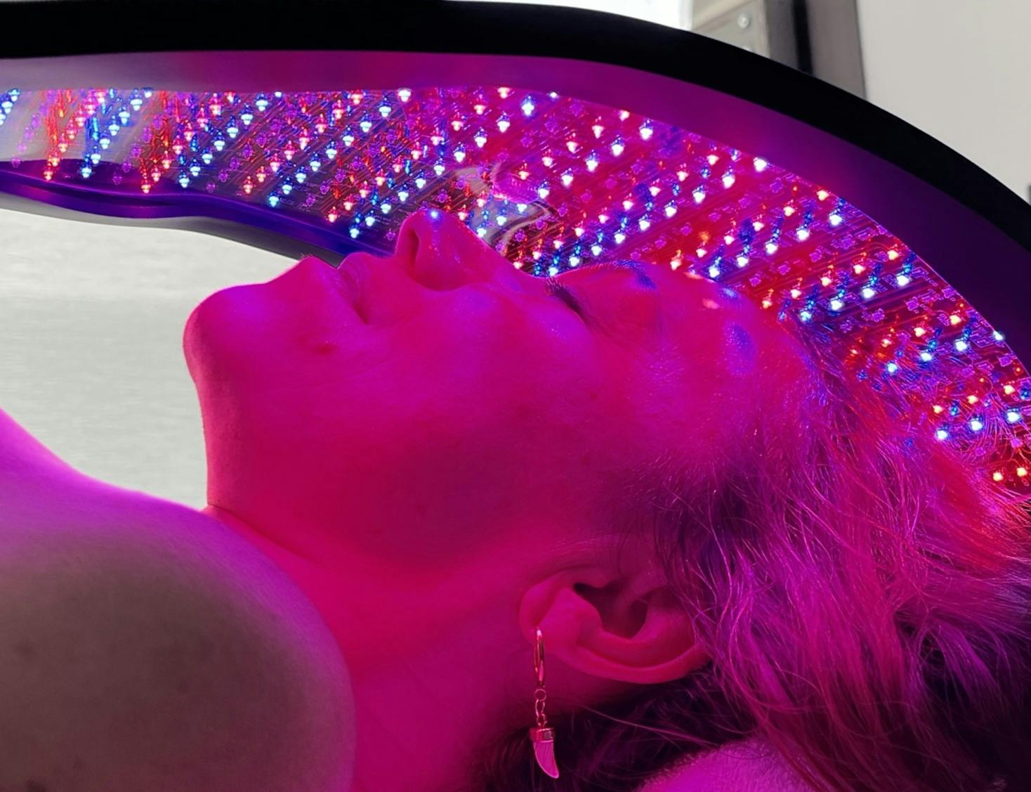 Close up of Stacey Morrison, host of Healthy or Hoax, lying under a Celluma light therapy device with red and blue lights on her face.