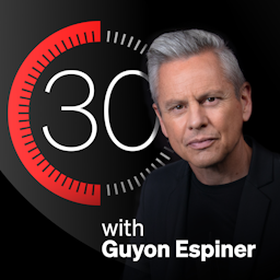 Guyon Espiner on a black background, looking at camera with logo behind him