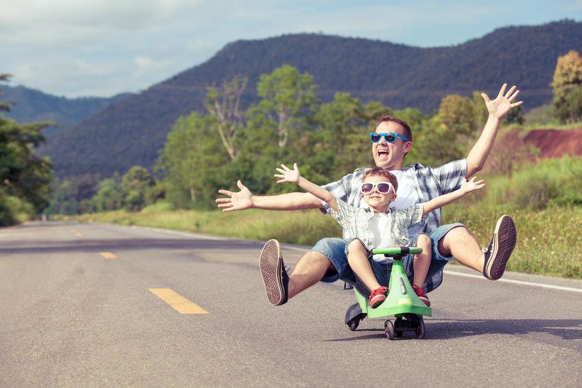 A photo of a father and son riding on a  skateboard playing on the road at the day time.