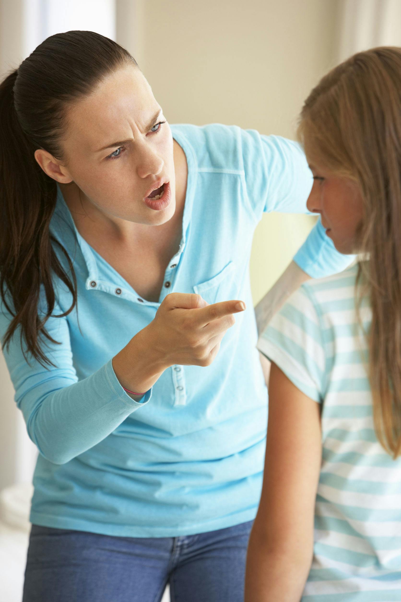 A close up image of an angry mother pointing her finger at her young daughter who looks chastened