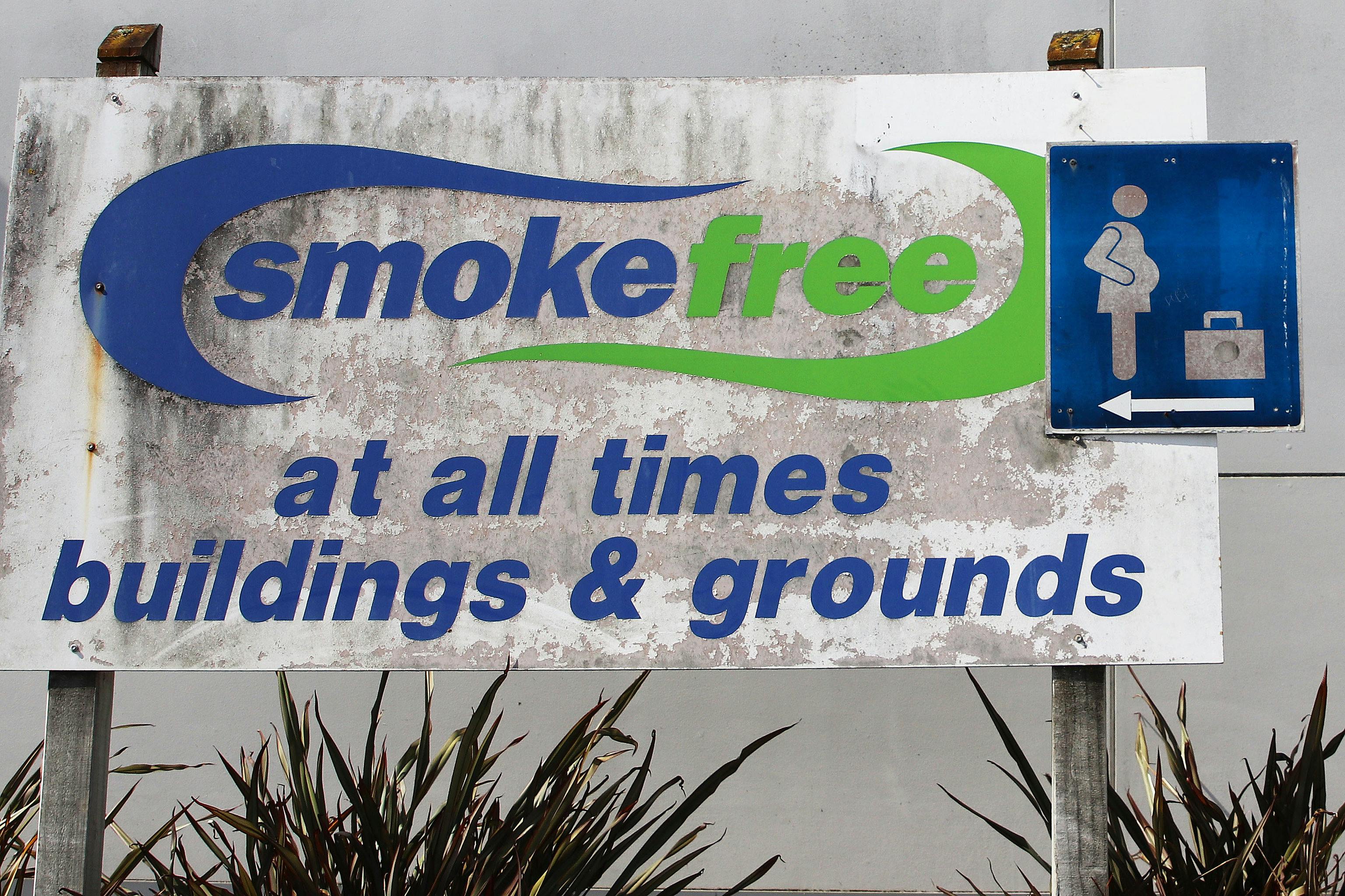 A dirty-looking Smokefree sign. It reads "SMOKEFREE - AT ALL TIMES - BUILDINGS & GROUNDS"