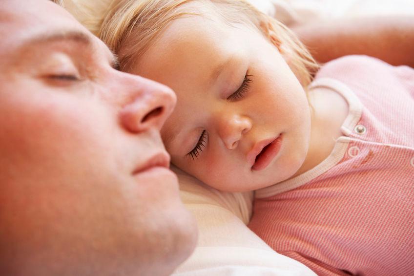 A photo of a father and daughter sleeping in bed