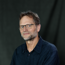 Image of Trevor Plant with a small smile in front of a dark grey background.