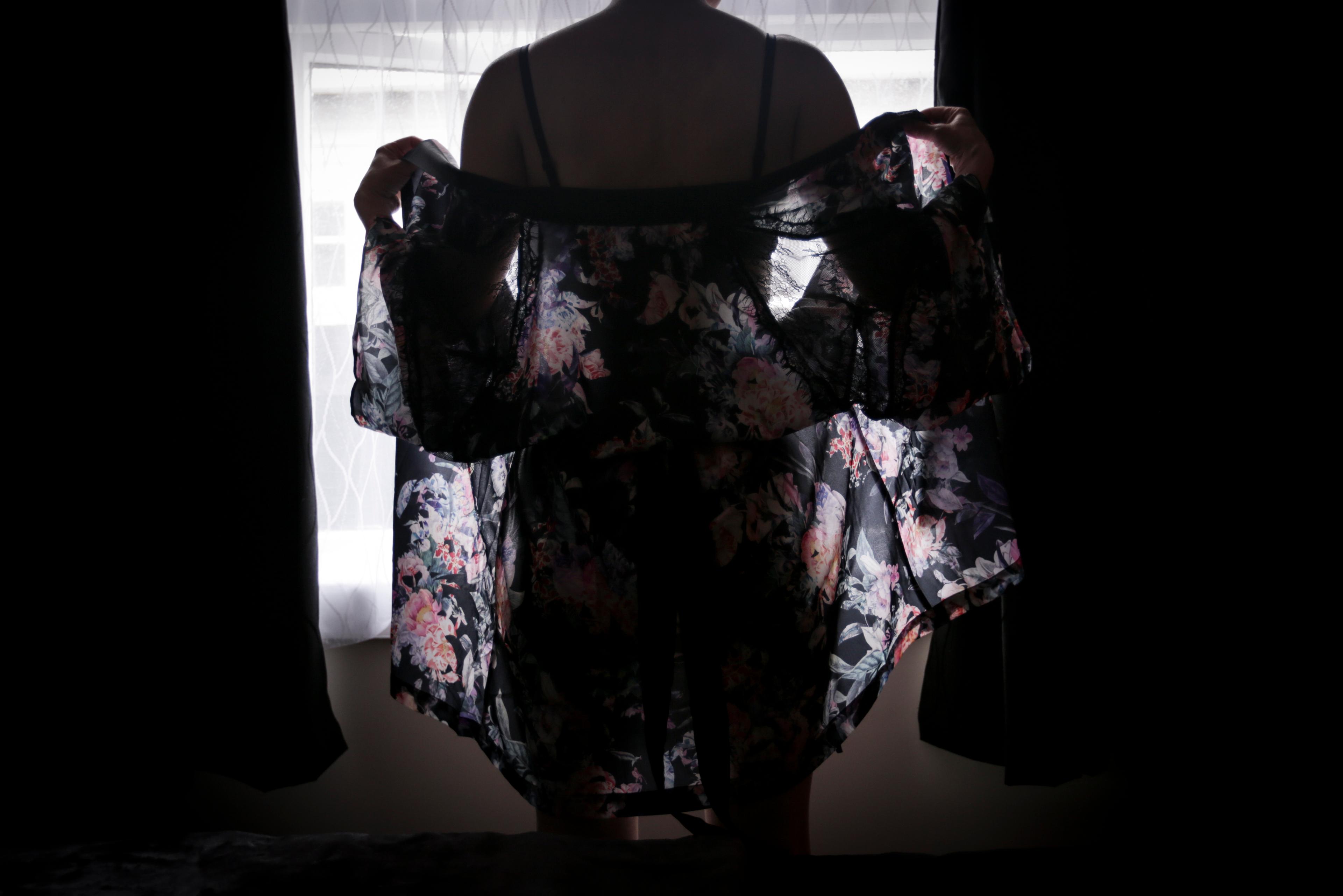 Woman stands silhouetted against window in lingeries and drapy wrap