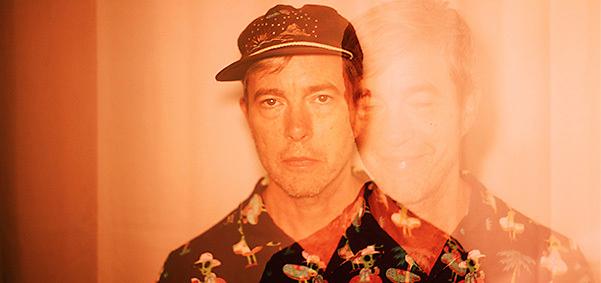 American musician Bill Callahan wearing a cap and patterned shirt in an image with an orange filter